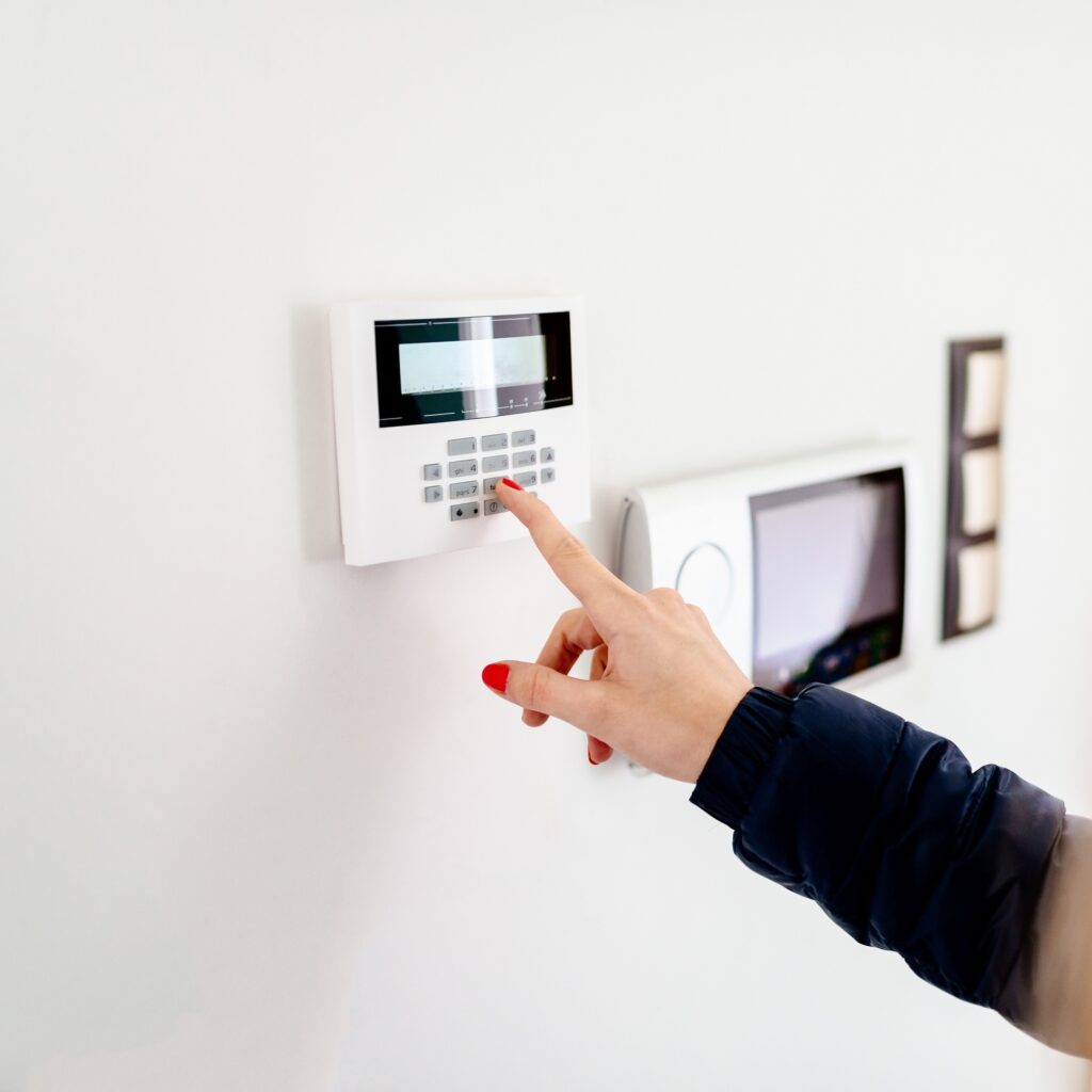 Main avec vernis rouge tapant un code sur le clavier d'un système d'alarme mural. Le doigt presse la touche 8 (tuv).