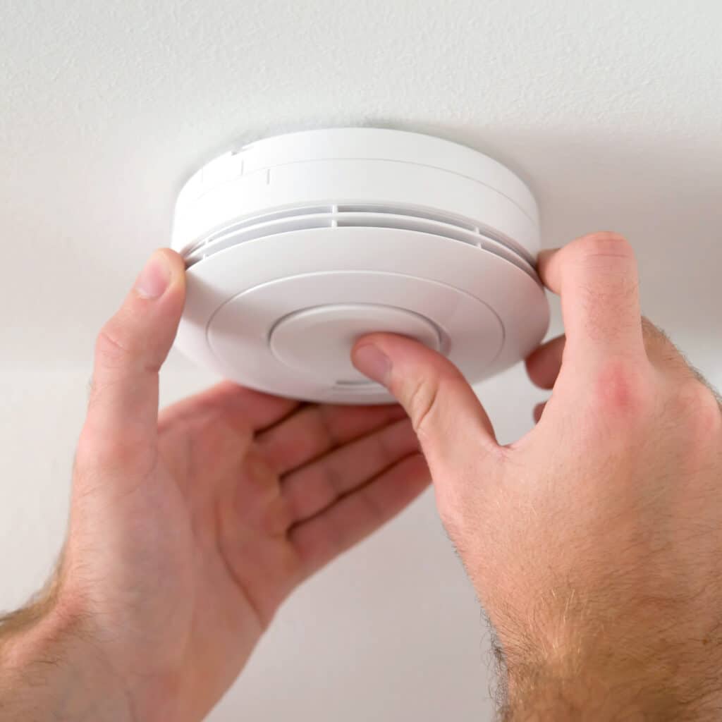 Mains pressant le bouton d'un détecteur de fumée blanc installé au plafond pour le tester ou le vérifier. Sécurité incendie domestique.